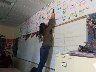 A senior student reaching high to put stars on a wall