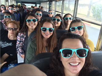 Lots of students on a school bus wearing sunglasses
